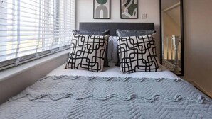 A bedroom with a bed, two pillows, a blanket, a window with blinds, and two wall art pieces. - Loft Living Leigh-on-sea (Leigh-on-Sea)