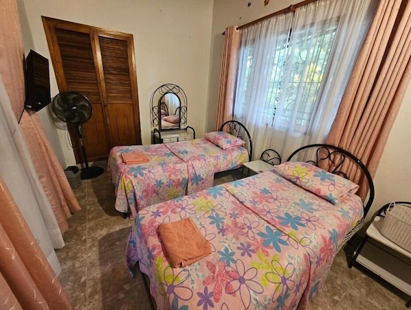 A bedroom with two beds, a mirror, a fan, and a window with curtains. - Twin Room - 2 single beds (Jagua)