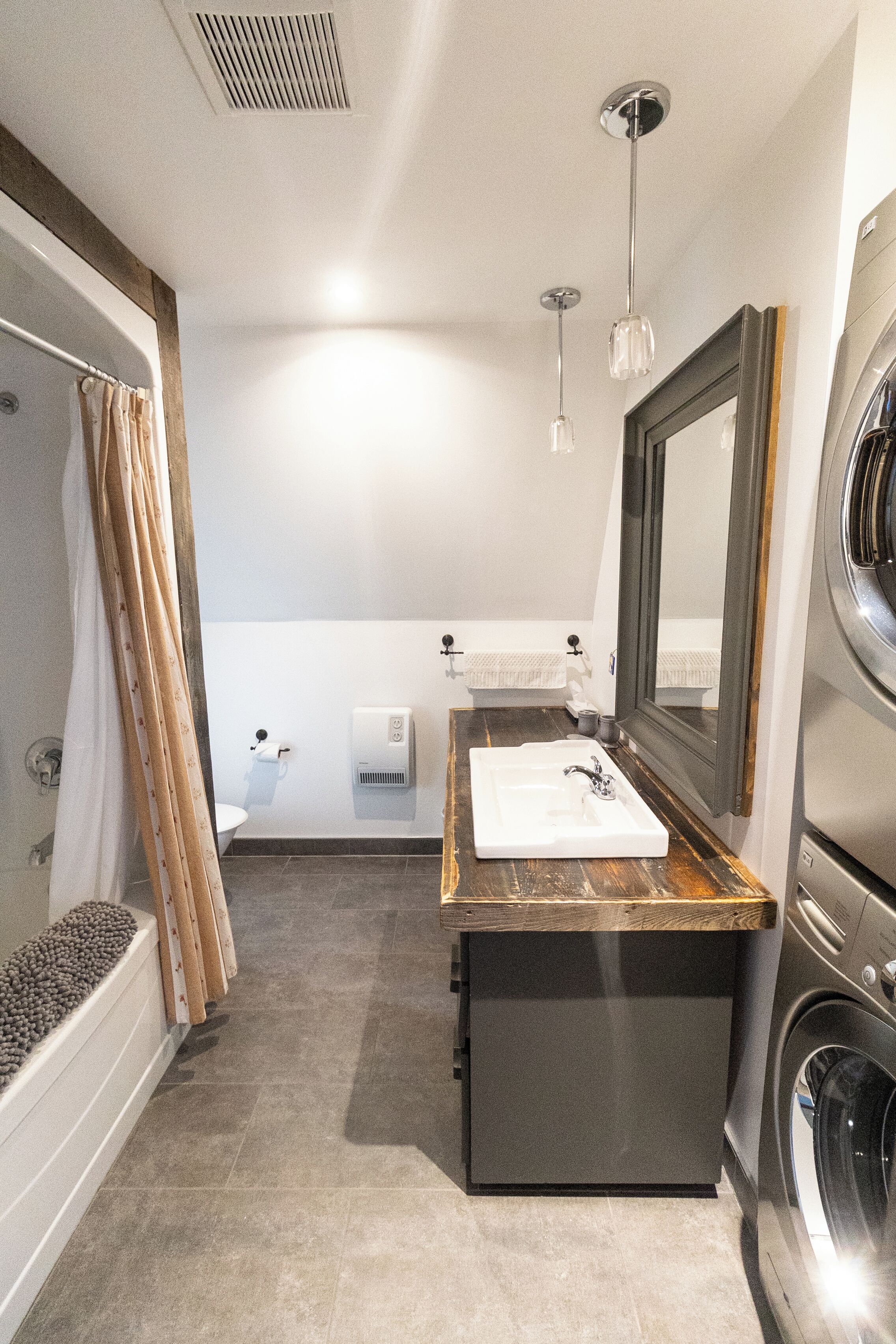 A modern bathroom with a sink, mirror, shower, and a washing machine.