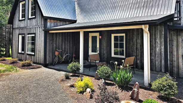 A two-story wooden house with a covered porch and a gravel driveway. - La Ruelle Hébergement (Saint-Siméon-de-Bonaventure)