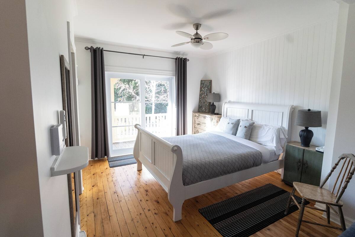 A bedroom with a bed, a nightstand, a chair, a ceiling fan, and a window with curtains.