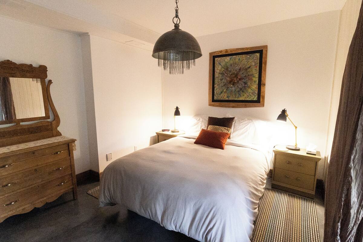 A bedroom with a large bed, wooden dresser, nightstands, and a hanging lamp.