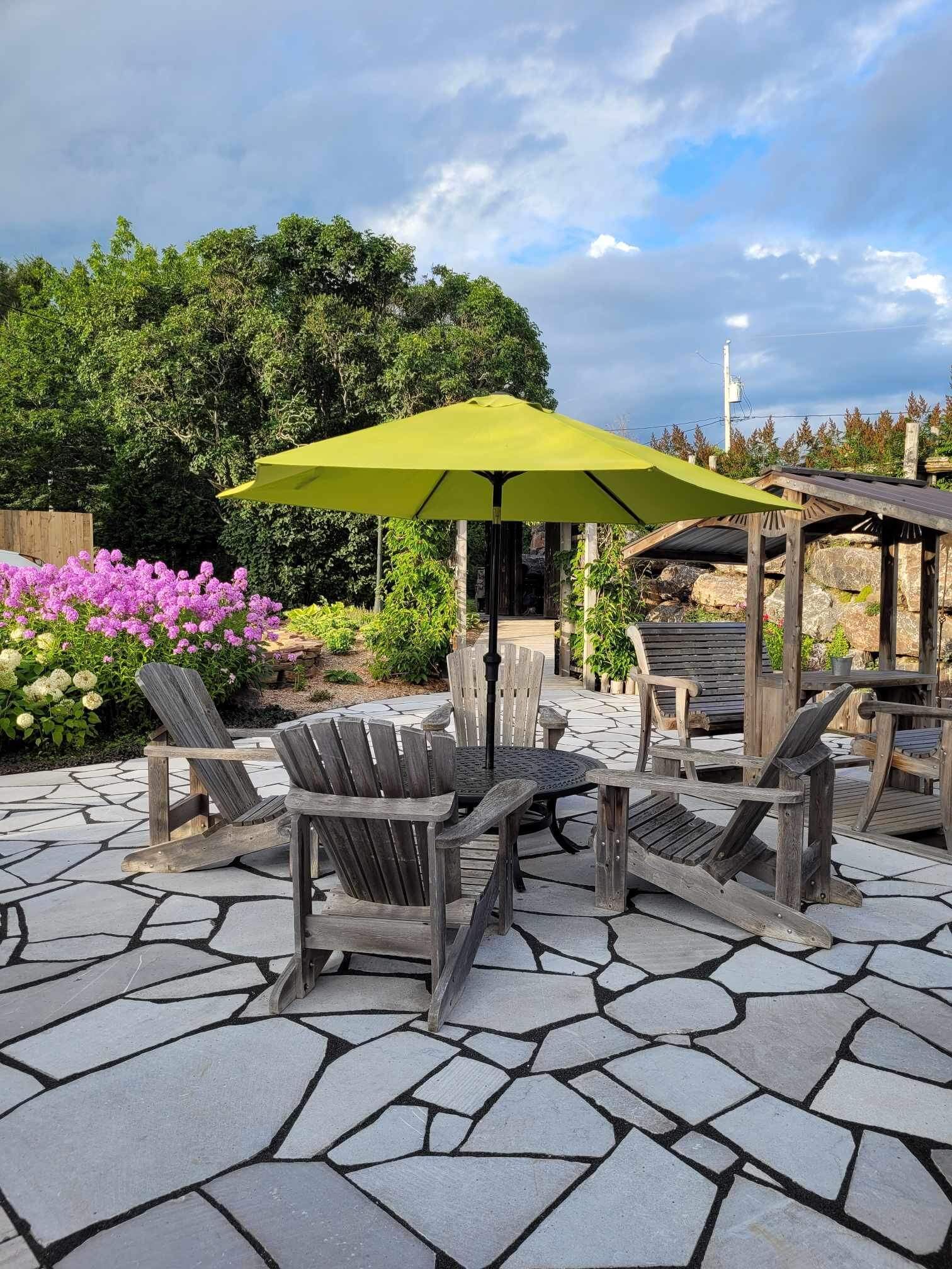 A patio area with Adirondack chairs, a round table, and a green umbrella.