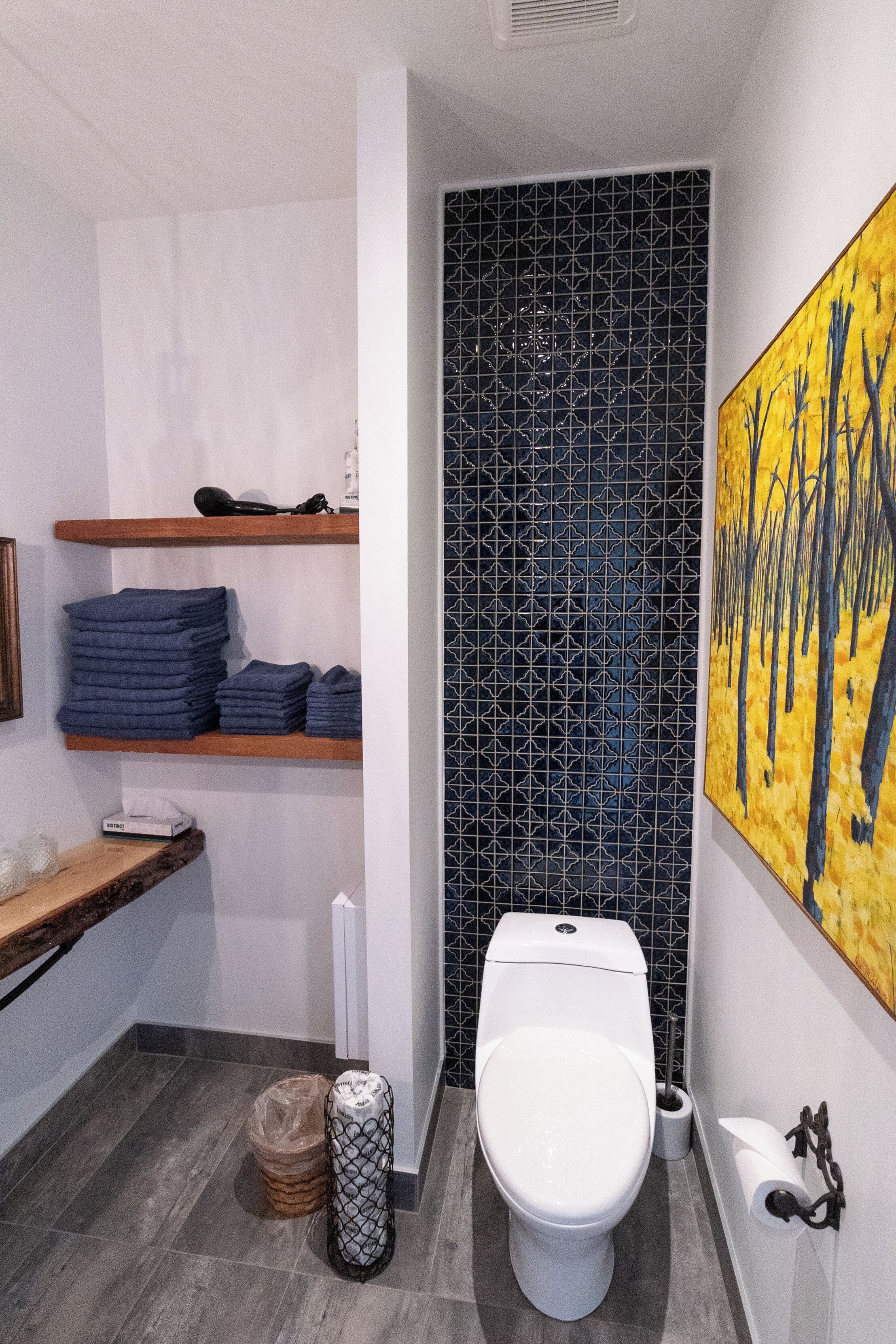 A modern bathroom with a toilet, a sink, and a shelf with folded towels.