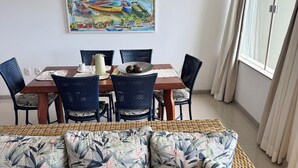 Un'area pranzo con un tavolo in legno, sedie blu e un divano in vimini con cuscini decorati.