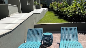Zona relax esterna moderna con due poltrone blu e un piccolo tavolino rotondo, circondata da un pontile in legno e un muretto basso.