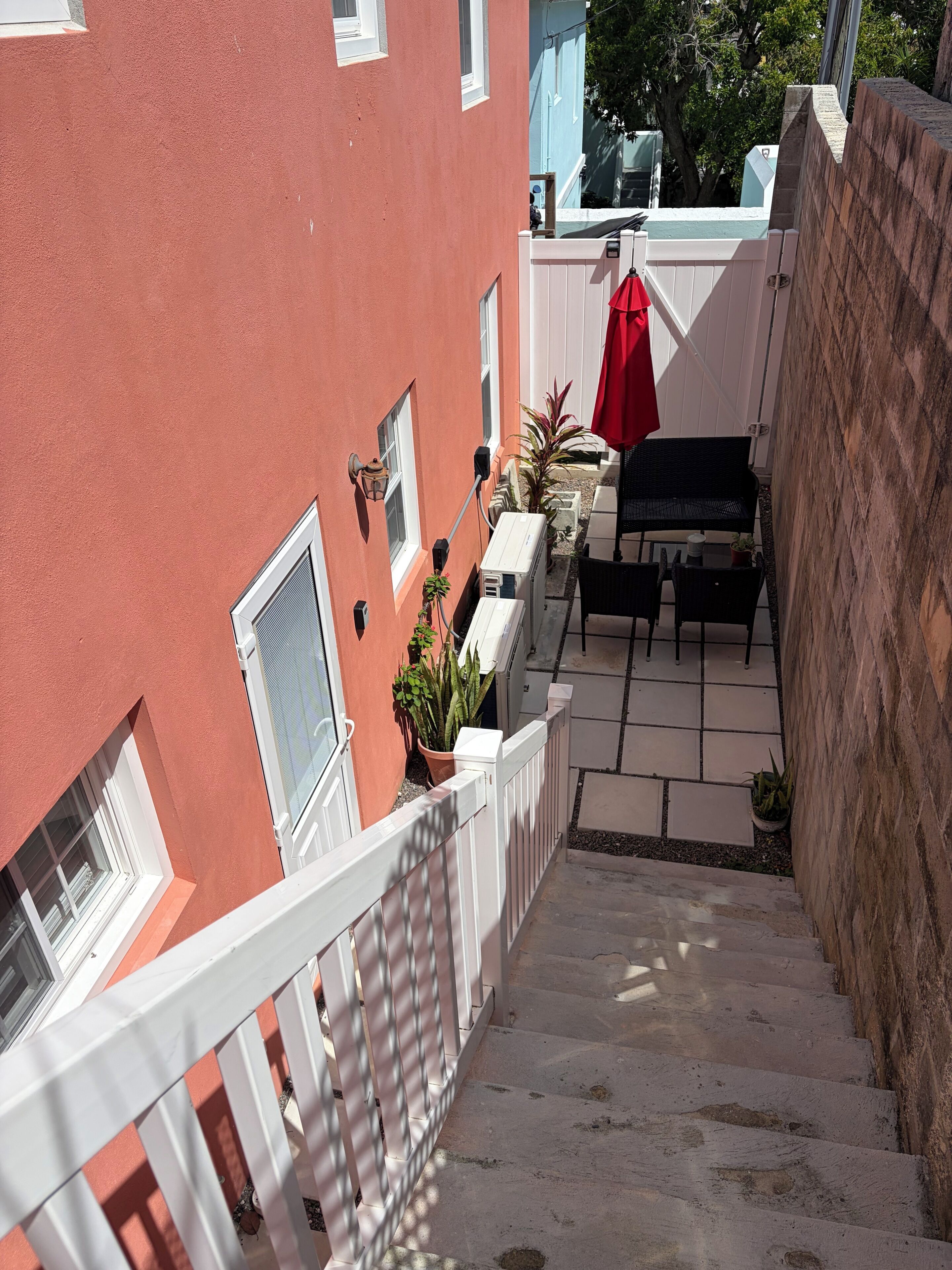 Un immeuble résidentiel à la façade rouge, avec une clôture blanche, un escalier menant à un balcon et du mobilier d’extérieur.