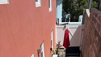 Un immeuble résidentiel à la façade rouge, avec une clôture blanche, un escalier menant à un balcon et du mobilier d’extérieur.