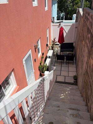 Ein Wohngebäude mit roter Fassade, weißem Zaun, einer Treppe, die zu einem Balkon führt, und Gartenmöbeln.