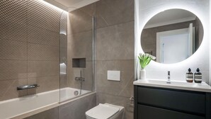 Un baño moderno con ducha de vidrio, inodoro blanco y tocador con espejo y dos botellas.