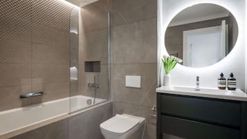 A modern bathroom with a glass-enclosed shower, a white toilet, and a vanity with a mirror and two bottles.