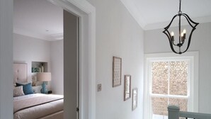 Una habitación con cama, un candelabro y ventana con vista a un muro de ladrillo.