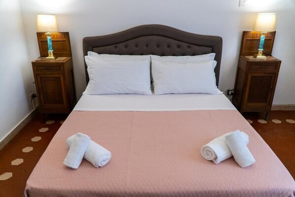 A neatly made bed with a pink bedspread and two white pillows, flanked by wooden nightstands with lamps. - Residence Le Cure (Florence)