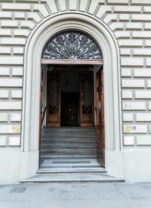 A building entrance with a grand archway, steps leading up to a wooden door, and a sign with numbers on the wall. - Residence Le Cure (Florence)
