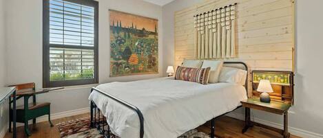A bedroom with a bed, a desk, a chair, a window with blinds, a ceiling fan, and a wall-mounted lamp.
