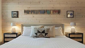 Ein Schlafzimmer mit einer Holzwand, einem Bett mit weißer Bettwäsche, zwei Nachttischen mit Lampen und einem an der Wand befestigten Messerhalter.