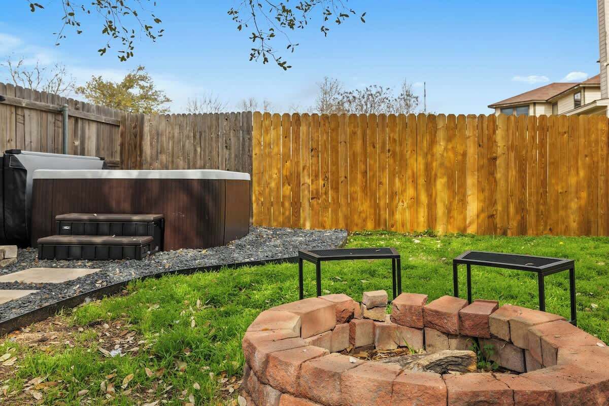 A backyard with a barbecue grill, a fire pit, and a wooden fence.
