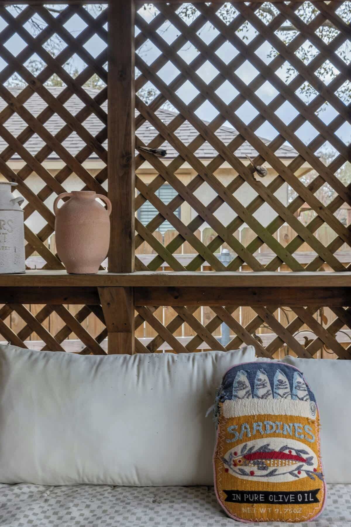 A wooden lattice structure with a white cushion and a decorative pillow with a fish pattern.