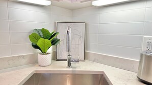 Een moderne keuken met een rvs spoelbak, witte marmeren aanrechtbladen en een potplant.