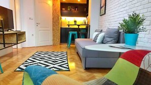 Un salon moderne avec un canapé gris, un fauteuil coloré, un tapis à motifs et une plante en pot.