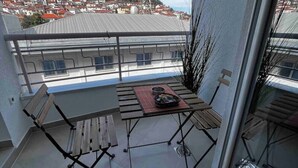 Un balcon avec une table et des chaises, une vue sur le paysage urbain et une haute tour de communication en arrière-plan.