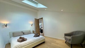 Ein modernes Schlafzimmer mit Bett, Sessel, Oberlicht und Spiegel.