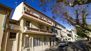 Ein mehrstöckiges Wohngebäude mit Balkon, ein Auto auf der Straße und Bäume mit Herbstlaub.