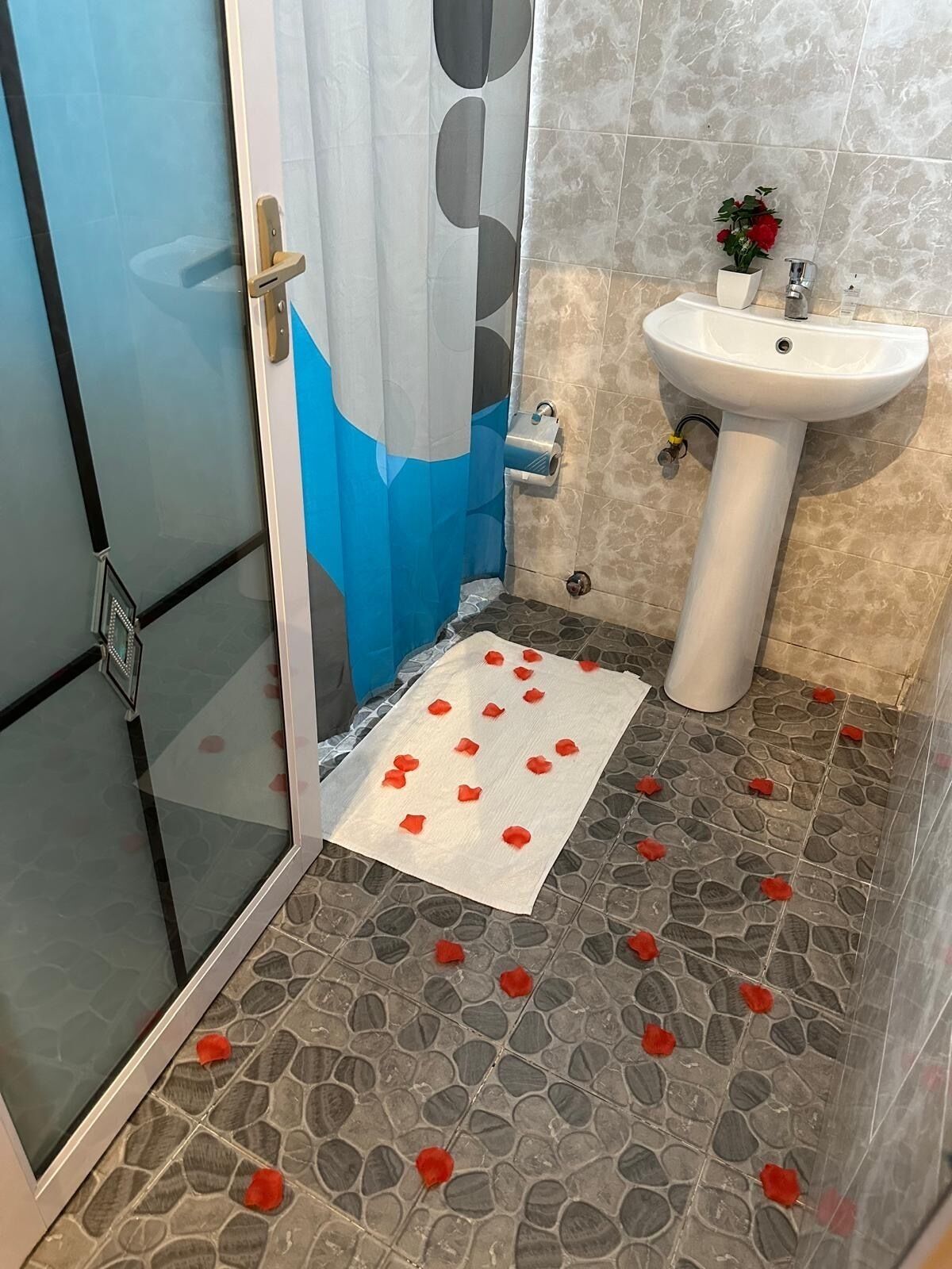 Un baño con mampara de vidrio, lavamanos blanco y piso estampado.