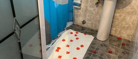 Un baño con mampara de vidrio, lavamanos blanco y piso estampado.
