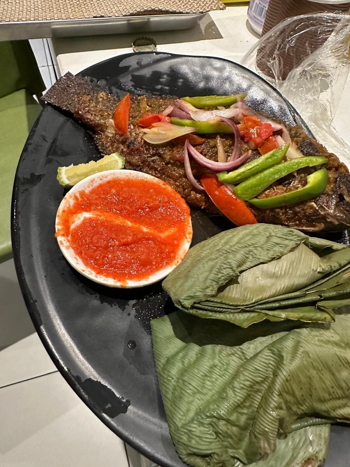 A plate with grilled fish, sliced vegetables, and a red sauce.