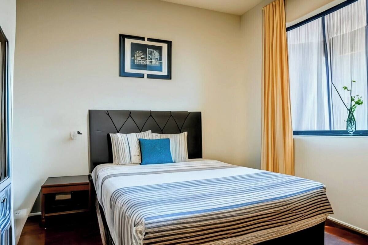 Una cama bien tendida con ropa de cama a rayas, un cabecero oscuro y un cuadro en la pared.