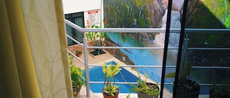 A view from a balcony with potted plants, a pool, and a mural of a natural landscape.