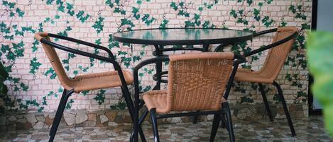 A round table with four wicker chairs, a brick wall with green ivy, and a stone-tiled floor.