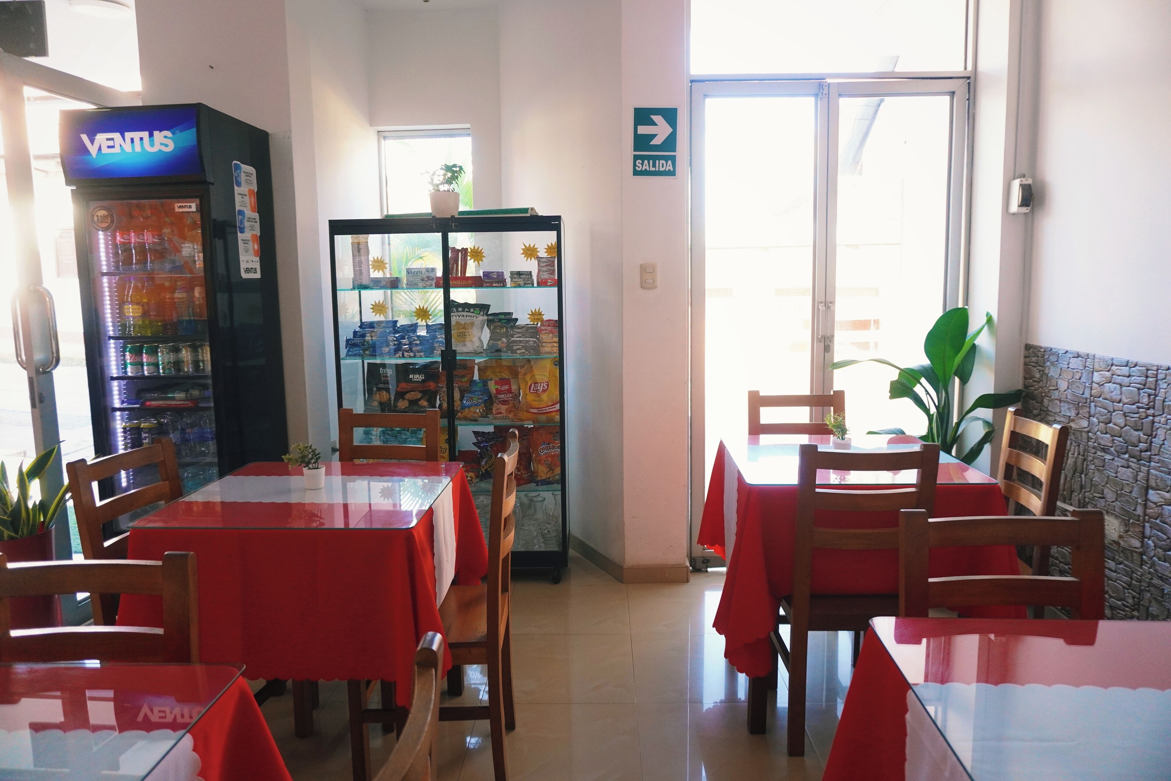 Een restaurant met rode tafelkleden, houten stoelen, een automaat en een glazen vitrine met snacks.