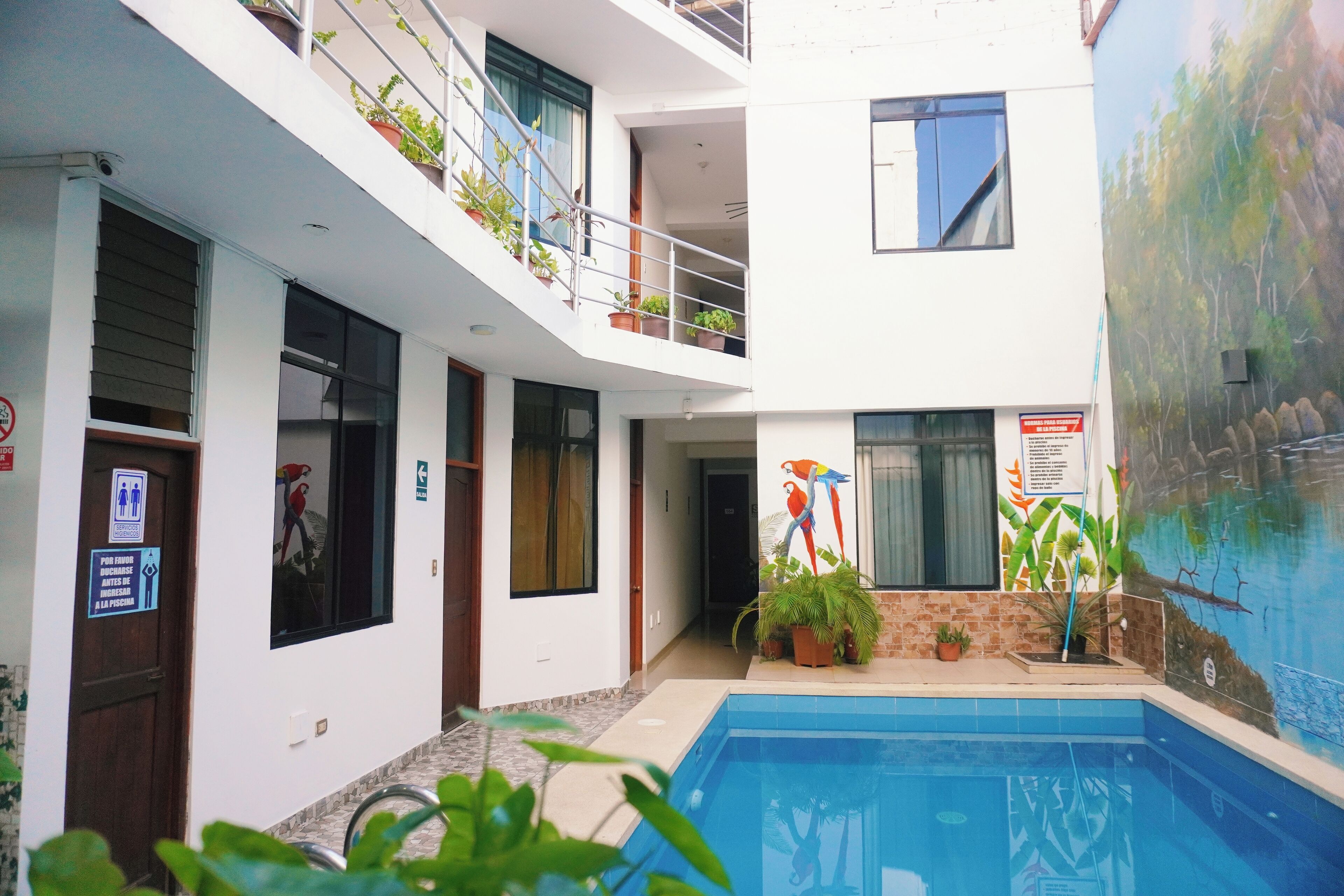 Un edificio moderno con piscina, balcones con plantas y un mural en la pared.
