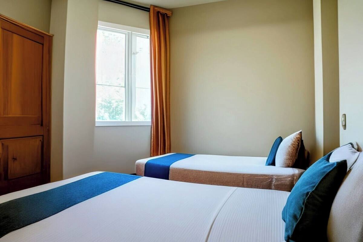 Habitación de hotel con dos camas, una ventana con cortinas y un armario.