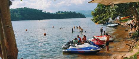 A lakeside scene with people swimming and jet skis docked along the shore.