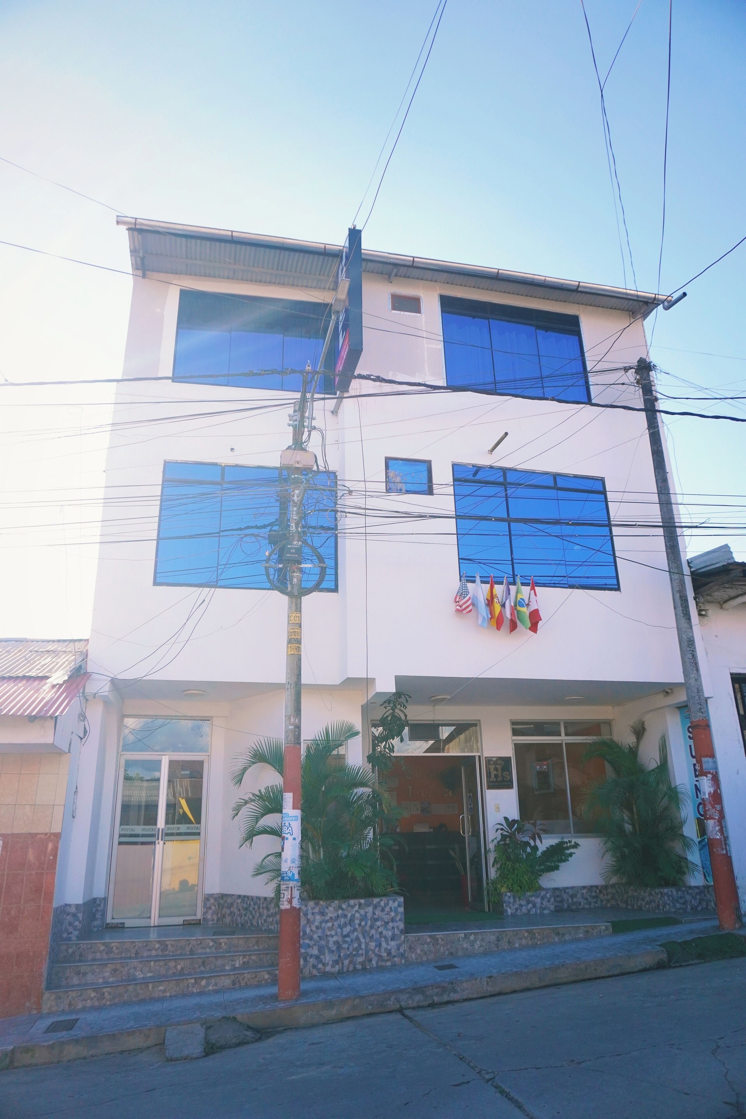 A two-story building with a white facade, large windows, and multiple flags.