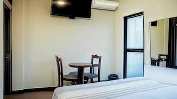 Una habitación de hotel con una cama, una mesita pequeña con dos sillas, un televisor de pantalla plana en la pared y una ventana con persianas.