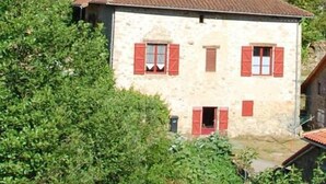 A stone house with red shutters, surrounded by greenery and a hill in the background. - Clos de l'ARTHONNET (Flavignac)