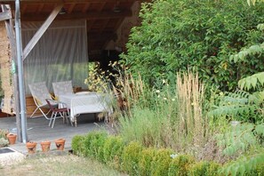 An outdoor seating area with a table and chairs, surrounded by lush greenery and a wooden deck. - Clos de l'ARTHONNET (Flavignac)