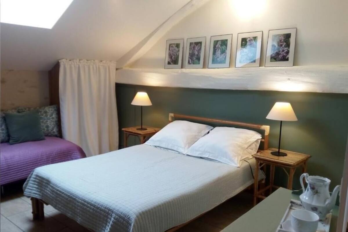 A bedroom with a bed, two bedside tables, a nightstand, a window with curtains, and a wall-mounted picture.