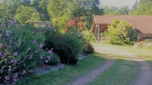 A rural house with a red-tiled roof, surrounded by lush greenery and flowering bushes. - Clos de l'ARTHONNET (Flavignac)
