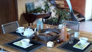 A dining table set with a teapot, cups, a basket of bread, and a bottle of water. - Clos de l'ARTHONNET (Flavignac)