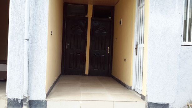 A hallway with two dark wooden doors, a tiled floor, and a white wall with a window on the right. - Liya Guest House  (Addis Ababa)