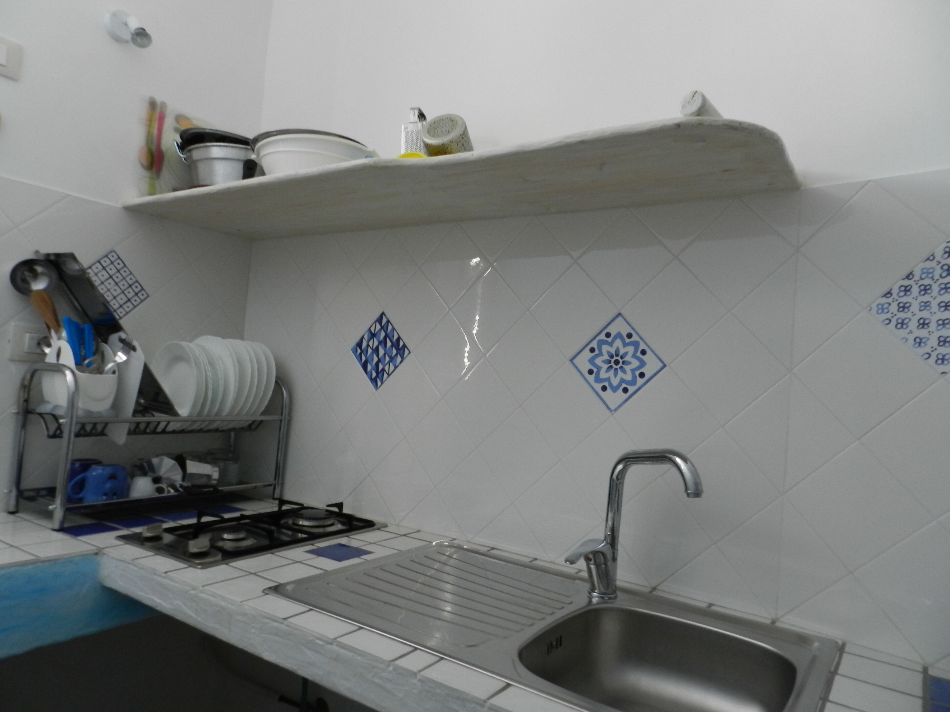 A kitchen with a stainless steel sink, a stove, and a shelf above the counter.