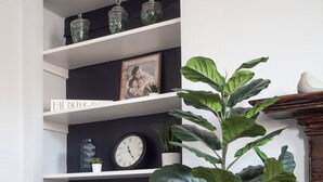 Une pièce avec un mur bleu foncé, des étagères blanches, une horloge et une grande plante en pot.