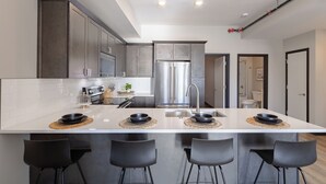 A modern kitchen with a large island, stainless steel appliances, and black bar stools.