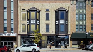 A multi-story building with a mix of commercial and residential spaces, featuring large windows and a prominent entrance with a green awning.