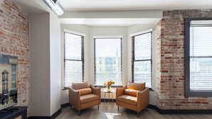 A modern living room with two leather armchairs, a small table with flowers, and large windows with blinds.